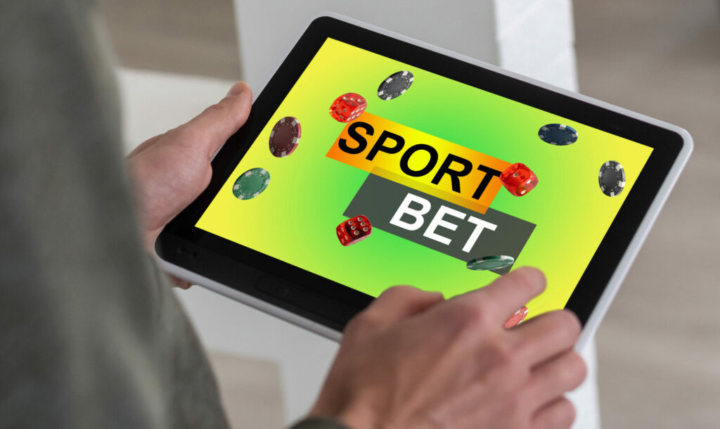 A man, out of frame, holding a tablet that reads "SPORT BET".