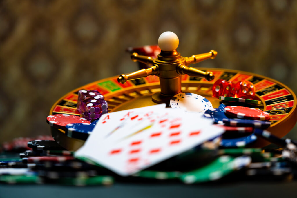 A photo of a roulette wheel with dice, casino chips and cards stacked on top.