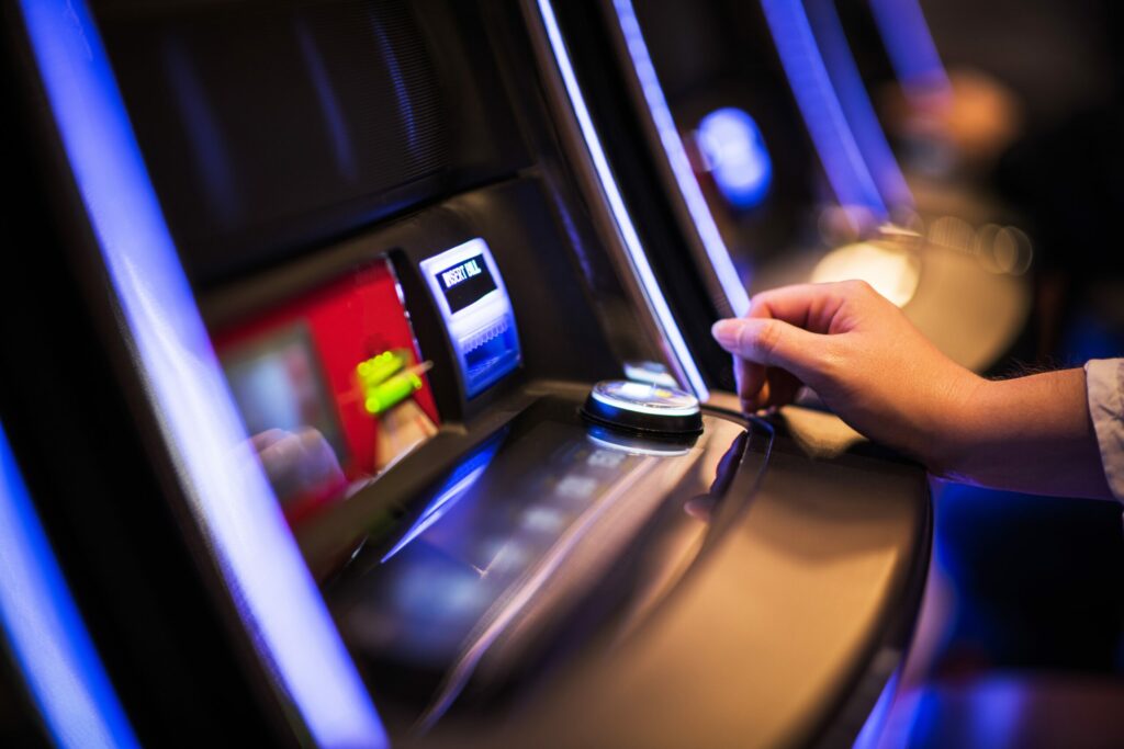 A photo of a person's hand next to a slot machine in a casino.