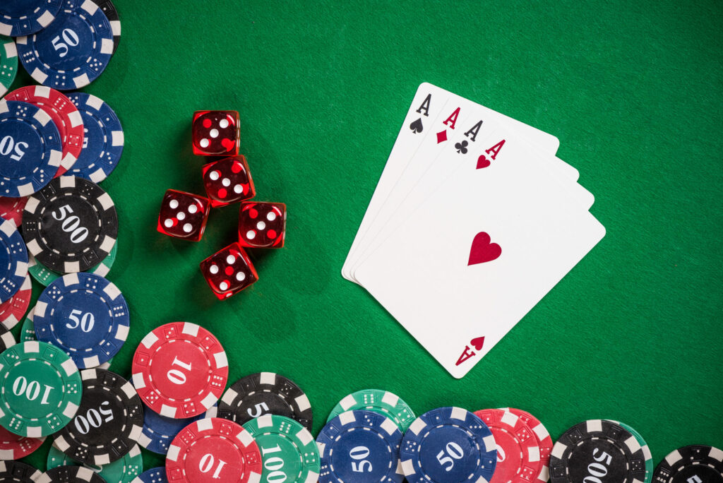 A photo of four Ace playing cards next to casino chips and dice.