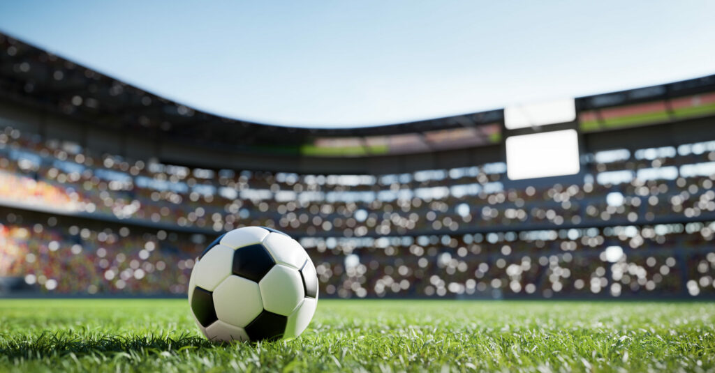 A photo of a football in the middle of a football pitch inside a football stadium.