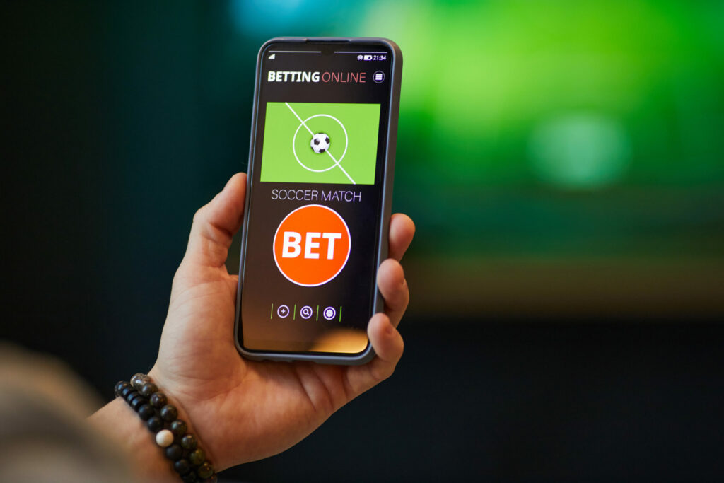 A photo of a person holding a phone with a betting app displayed on the screen.