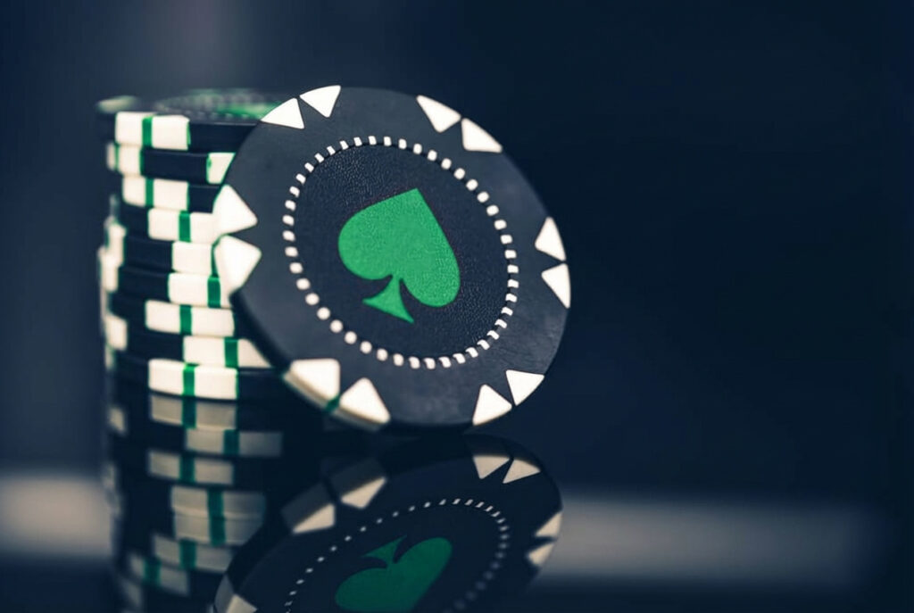 A pile of mostly black chips with white and green accents. One chip leans against the pile, with a green spade at its centre.