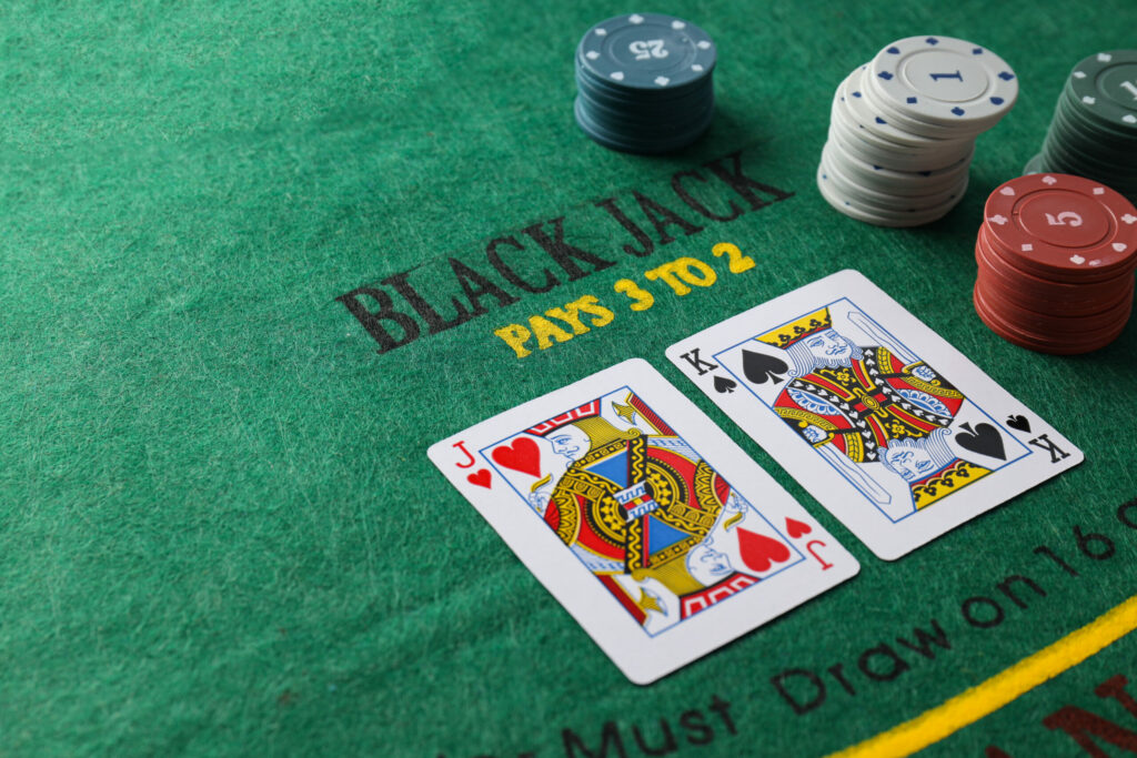 Green blackjack table with casino chips and two cards, the Jack of Hearts and the King of Spades, on it.