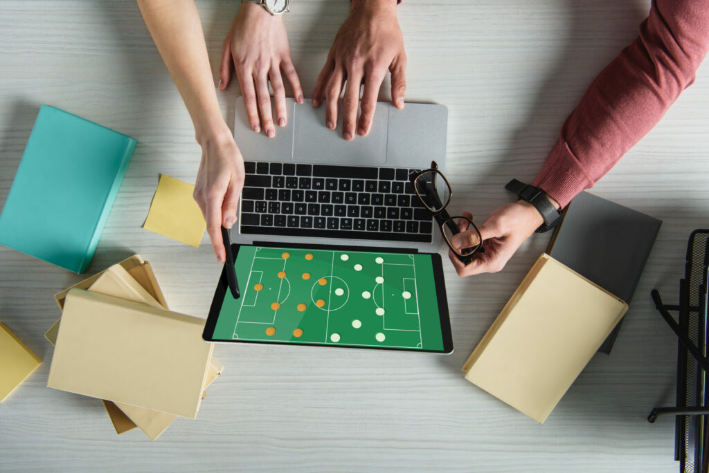 A cropped view of woman pointing at laptop with a football pitch illustration onscreen, with dots to represent each team's formation, near a man holding glasses.