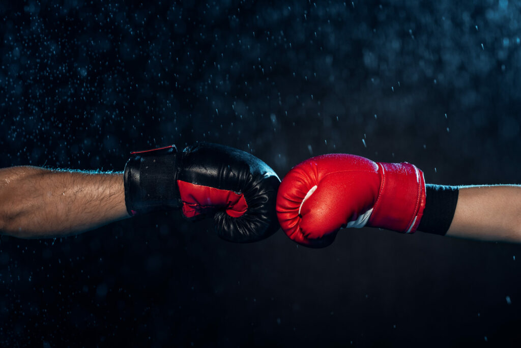 Partial view of two boxers in boxing gloves touching fists on a black background.