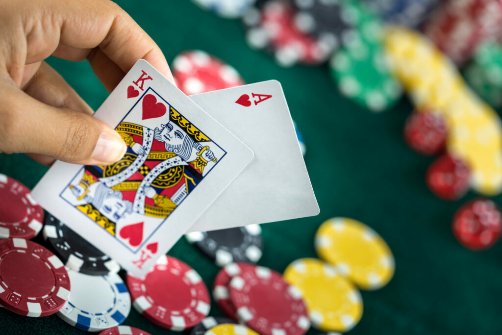 Hand holding a King of Hearts and an Ace of Hearts. Casino chips appear in the background on a green table, blurred.