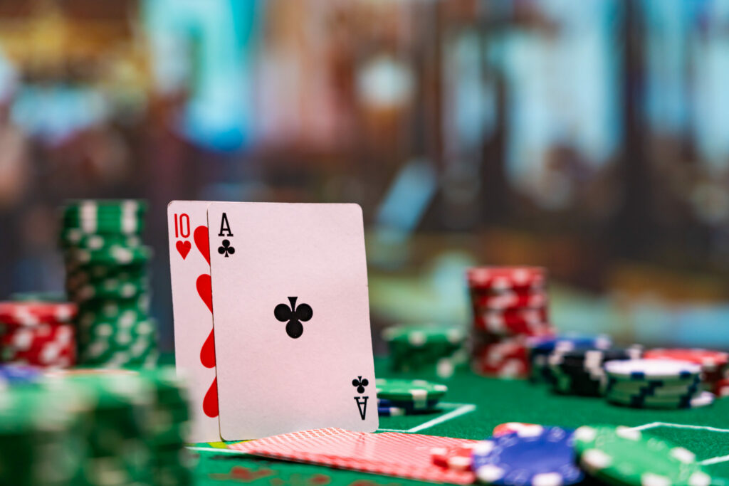 An Ace of Clubs and a 10 of Hearts standing upright on a green blackjack table. There are casino chips around them, but they're blurred, as is the background.
