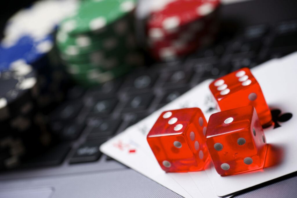 Dice, cards and poker chips on a keyboard. The casino chips, keyboard and part of the cards and dice are blurred.