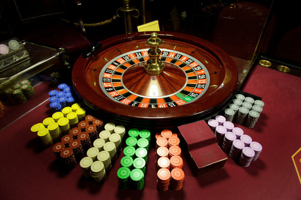 Close-up of casino chips and a roulette wheel at a casino on a red table.