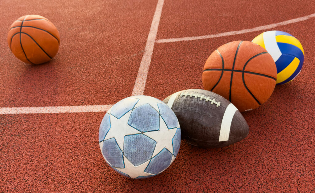 A collection of sports balls, including a football, an American football, a volleyball, and two basketballs.