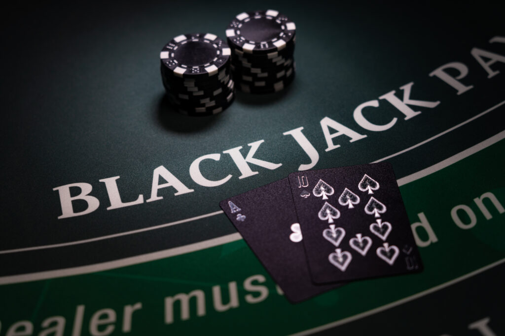Two black playing cards, an Ace of Clubs and a 10 of Spades, and two stacks of black casino chips on a blackjack table.