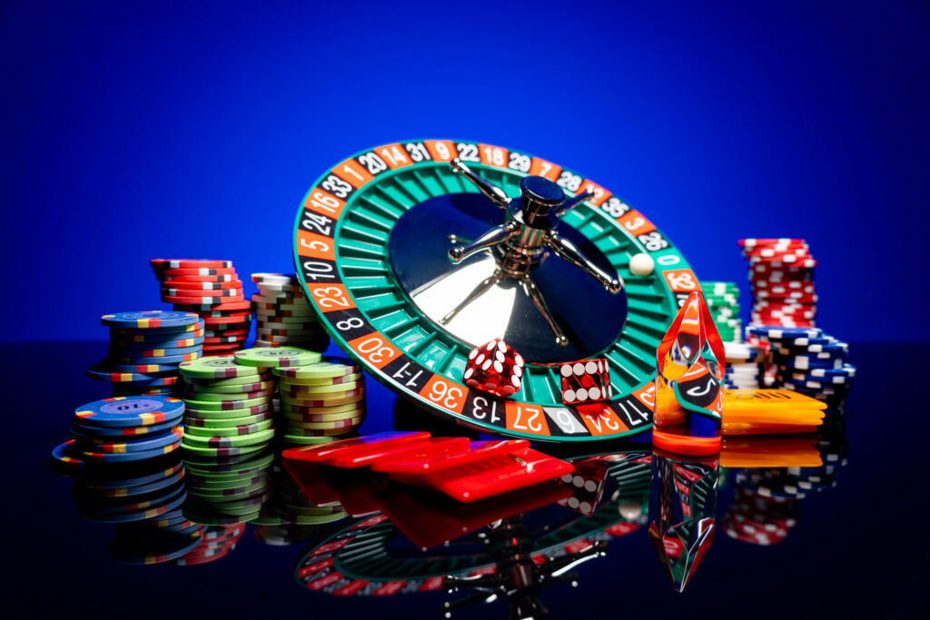 A roulette wheel with a ball in it on zero and red dice in the 13 and 34 slots. Beside it are different types and stacks of casino chips.