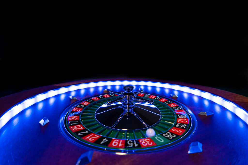Close up of a roulette wheel with a black background. The wheel is lit up with cool blue lighting.