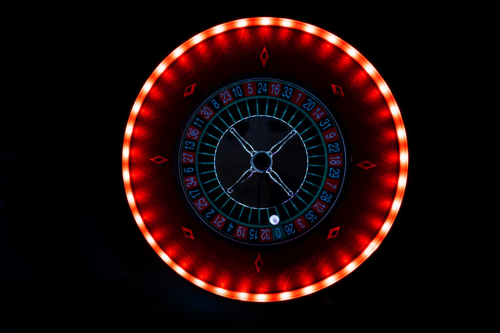 Close up of a roulette wheel at a casino. Edge of wheel is lit up whilst the majority of the image is dark or dim.