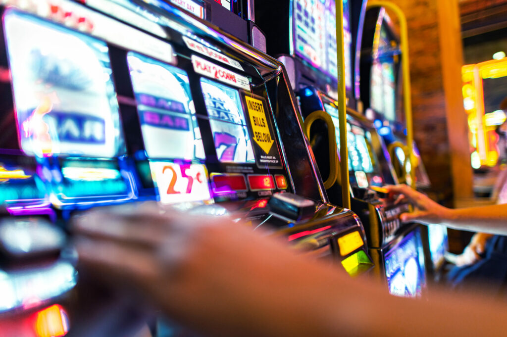 Close up of slot machines in a casino with players on them (only their hands are in the image).