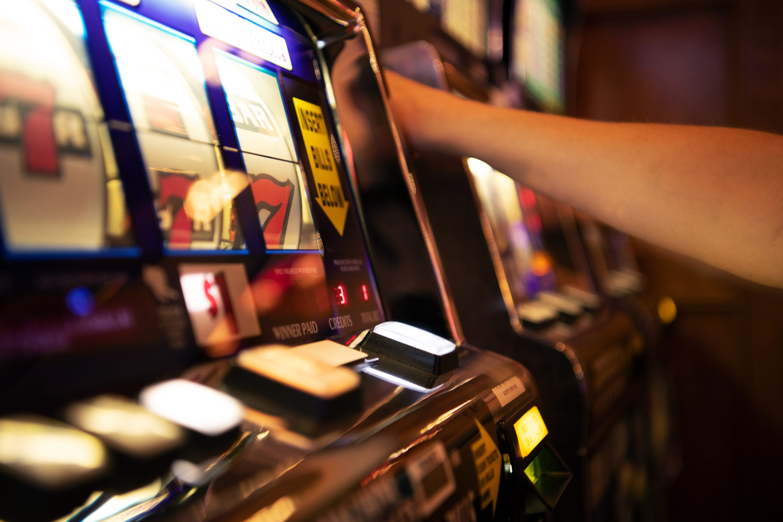 A person playing a slot machine in a casino (only their arm is in frame).